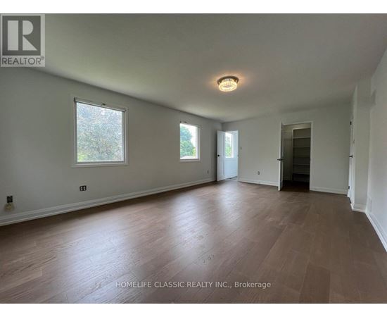 A room with wooden flooring and white walls, with a window on the left wall.