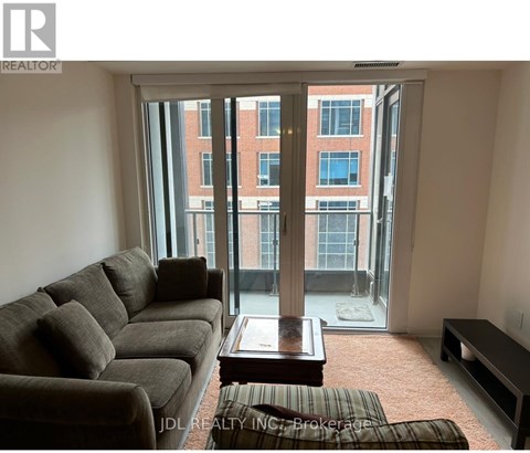 A living room with a couch, coffee table, and a view of a building through the window.
