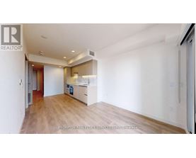 A spacious room with wooden flooring and white walls, featuring a kitchen area with white cabinets and appliances.