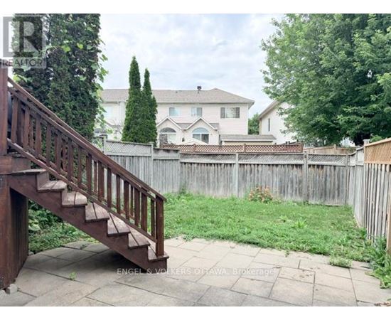 A wooden staircase leads to a house with a white fence and green trees in the background.