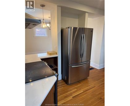 A stainless steel refrigerator stands in a kitchen with wood floors.