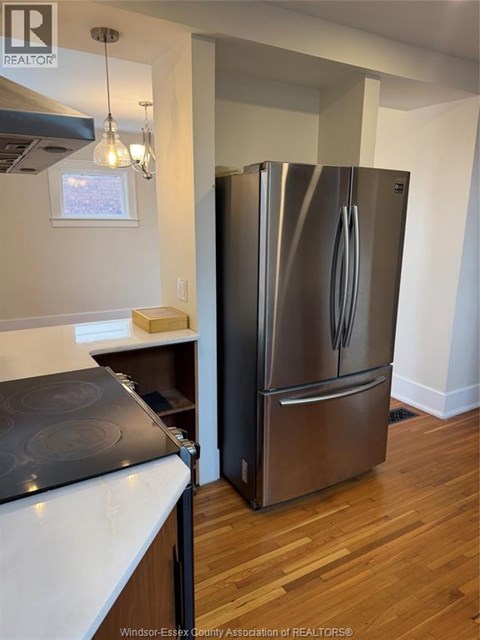 A stainless steel refrigerator stands in a kitchen with wood floors.