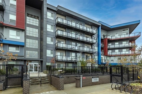 A modern apartment building with a black fence and bicycles parked in front.
