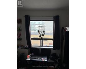 A window with a view of a cityscape is framed by a window seat with a laptop and a pair of headphones hanging from it.