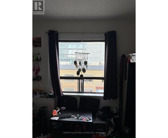 A window with a view of a cityscape is framed by a window seat with a laptop and a pair of headphones hanging from it.