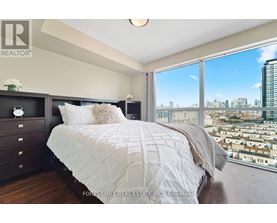 A bedroom with a large bed and a city view through the window.