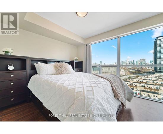 A bedroom with a large bed and a city view through the window.
