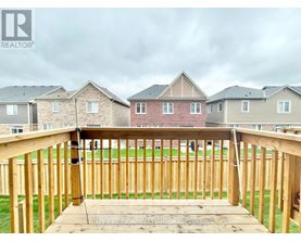 A wooden deck with a railing in the foreground and houses in the background.