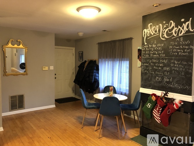 A room with a dining table and chairs, a mirror, and a chalkboard with writing on it.