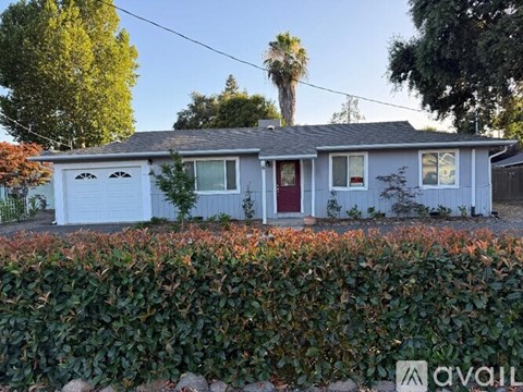 A house with a red door is surrounded by a hedge.