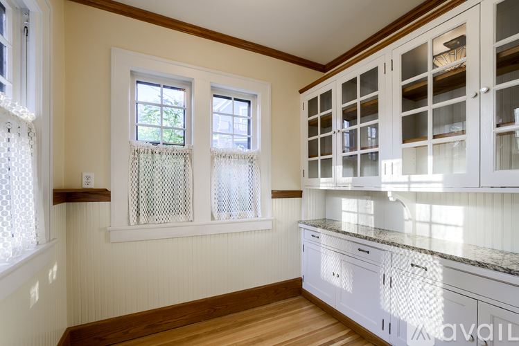 A kitchen with white cabinets and a window with a white curtain.