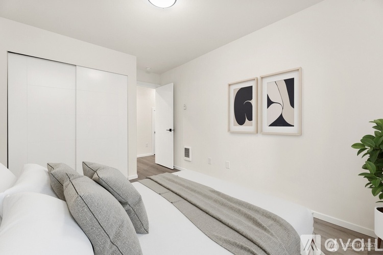 A bedroom with a bed, pillows, a blanket, and two framed artworks on the wall.