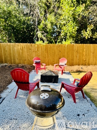 A BBQ grill is in the middle of a patio with four chairs around it.