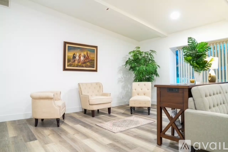 A living room with a painting on the wall, two chairs, a desk, and a couch.