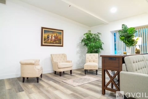 A living room with a painting on the wall, two chairs, a desk, and a couch.
