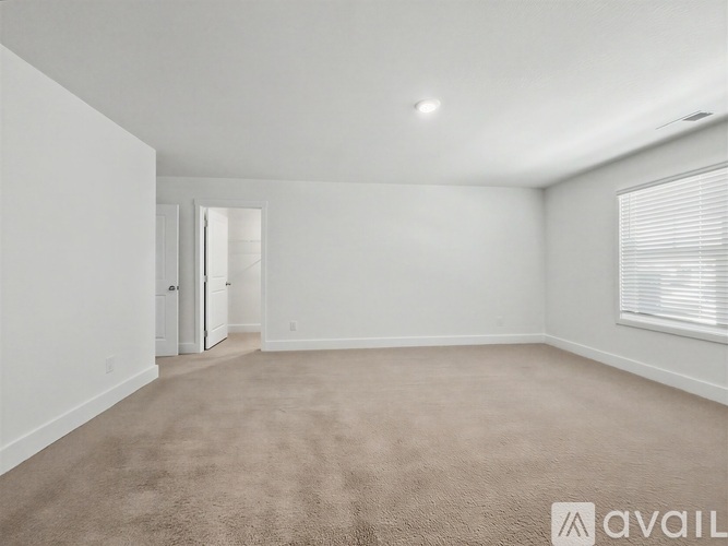 A spacious room with beige carpeting and white walls, featuring a doorway leading to another room.