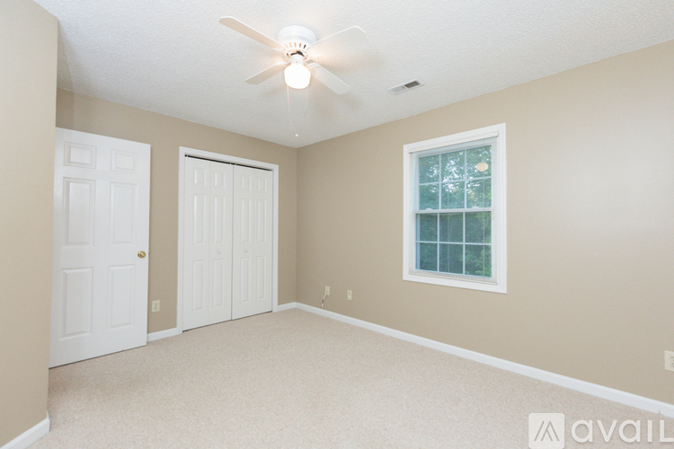 A room with a ceiling fan and a window with a view of trees.