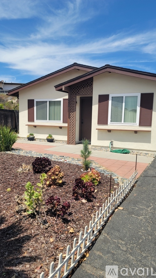 A house with a brown roof and white walls has a small garden in front.