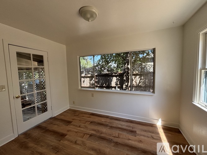A room with wooden floors and a large window with a view of trees.