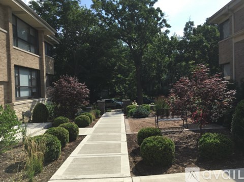 A concrete walkway leads through a landscaped area with bushes and trees.