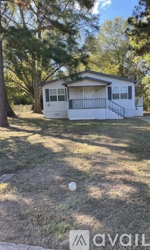 A house with a white exterior and a black railing is surrounded by trees.