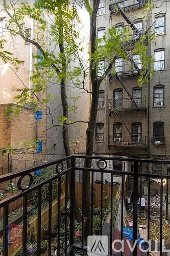 A balcony with a black railing and a tree in front of a building.