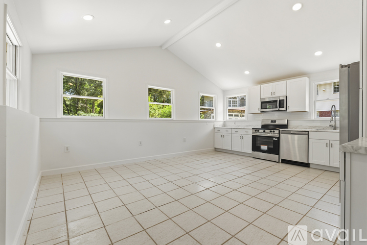 A spacious kitchen with white cabinets and appliances, a tiled floor, and a window with a view of trees.