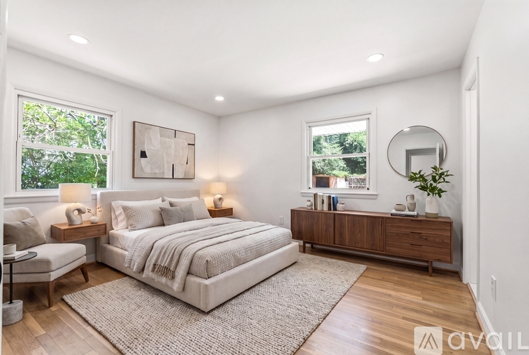 A bedroom with a large bed, a chair, a side table with lamps, and a wooden dresser.