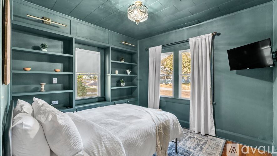 A bedroom with a bed, a window, and a TV mounted on the wall.