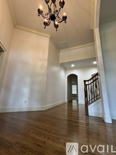 A large, empty room with a wooden floor and a chandelier hanging from the ceiling.
