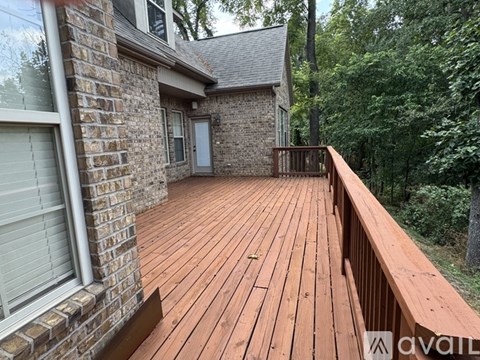 A wooden deck with a brick house and trees in the background.