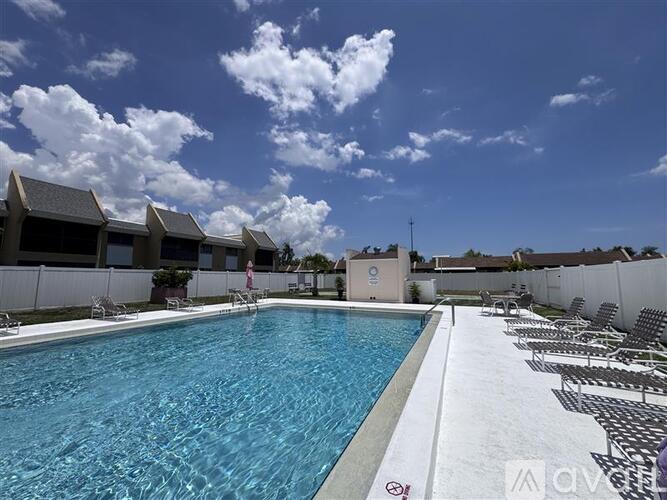 A large swimming pool with a white fence and black and white striped lounge chairs.