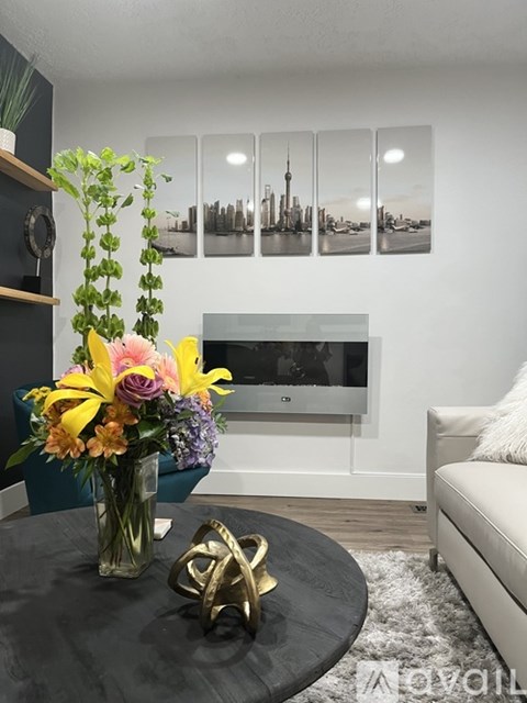 A living room with a TV, a couch, a table with a vase of flowers, and pictures on the wall.