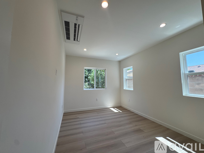 A spacious room with wooden flooring and a window overlooking a tree-filled outdoor area.