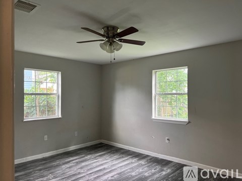 A room with a ceiling fan and two windows.