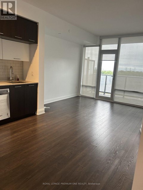 A spacious room with wooden flooring and a kitchen area with white cabinets and black appliances.