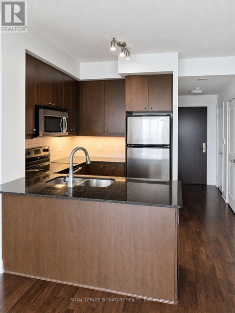 A modern kitchen with dark wood cabinets and stainless steel appliances.