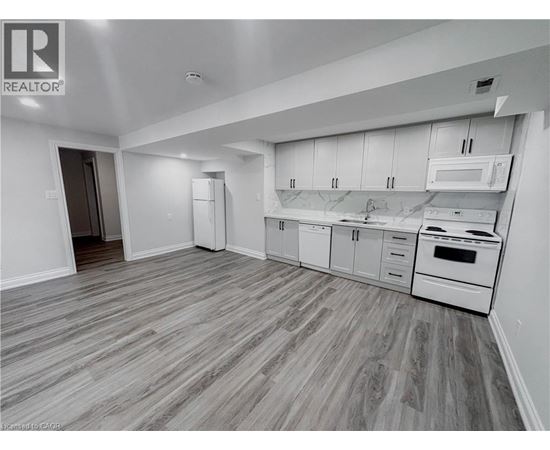 A spacious kitchen with white appliances and wooden flooring.