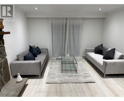 A modern living room with a glass coffee table and two grey sofas.