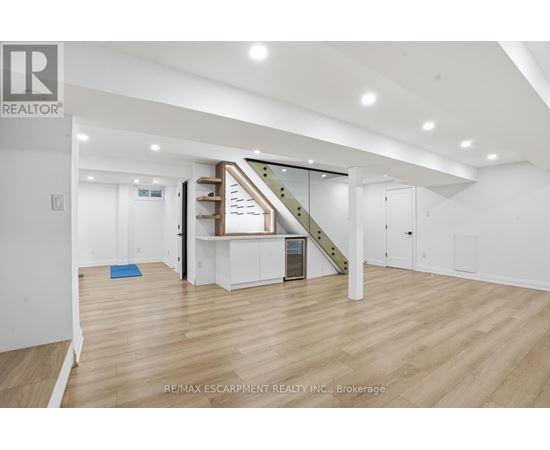 A spacious room with wooden flooring and a staircase with a glass railing.