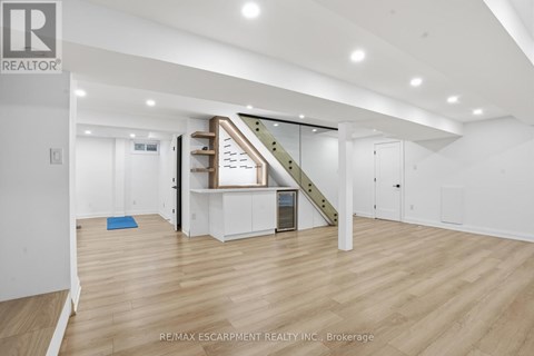 A spacious room with wooden flooring and a staircase with a glass railing.