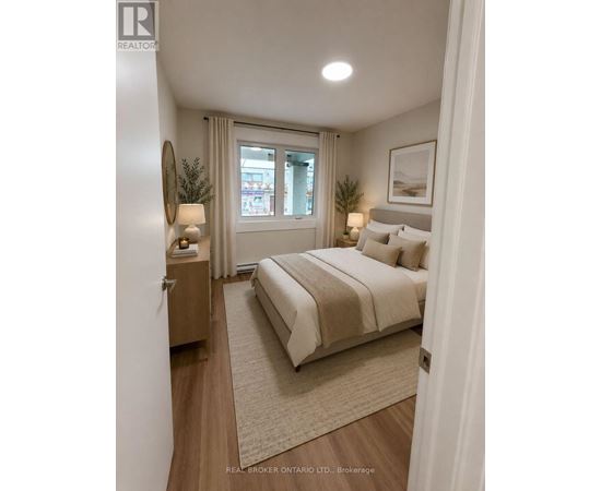 A bedroom with a large bed, a nightstand with a lamp, and a framed picture on the wall.