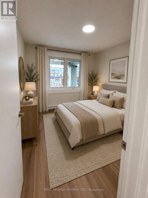 A bedroom with a large bed, a nightstand with a lamp, and a framed picture on the wall.