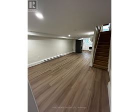 A spacious room with wooden flooring and a staircase on the right side.