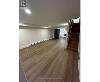 A spacious room with wooden flooring and a staircase on the right side.