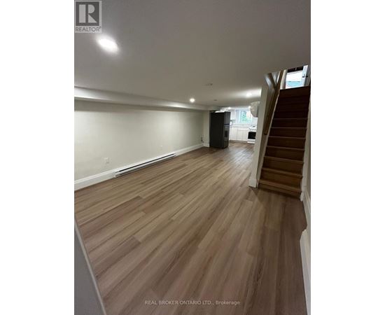 A spacious room with wooden flooring and a staircase on the right side.