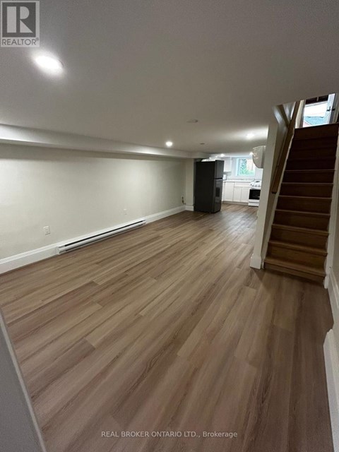 A spacious room with wooden flooring and a staircase on the right side.