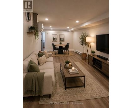 A room with wooden flooring and a white wall with a Real Broker logo.