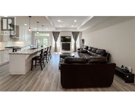 A modern living room with a brown leather couch and a kitchen area with white cabinets.