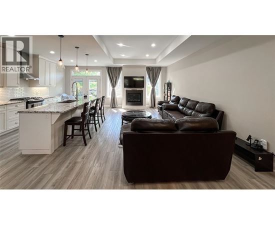 A modern living room with a brown leather couch and a kitchen area with white cabinets.